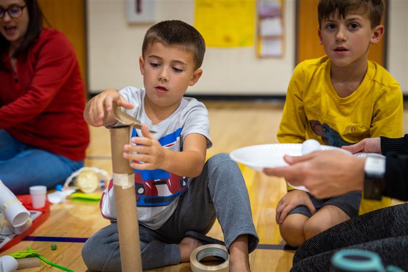 A boy wearing a white shirt drops marbles down a paper rollercoaster